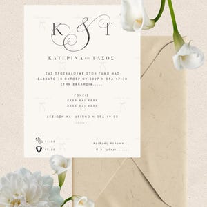May include: A white wedding invitation card with black text and a large K & T monogram, featuring Greek text, icons of high heels and a tuxedo, and white calla lilies. The invitation is placed next to a tan envelope on a textured background.