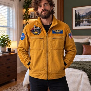 May include: A mustard yellow corduroy jacket featuring a full-length front zip, two chest pockets, and various patches. The patches include a circular NASA logo, a Project Aobe mission emblem, a blue name tag reading Grace, and a US flag patch.