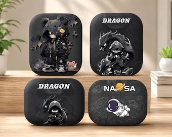 May include: Four black protective cases for wireless earbuds. The top left case features a bear character in a hoodie. The top right and bottom left cases display a dragon and the text DRAGON. The bottom right case shows an astronaut and the text NASA.