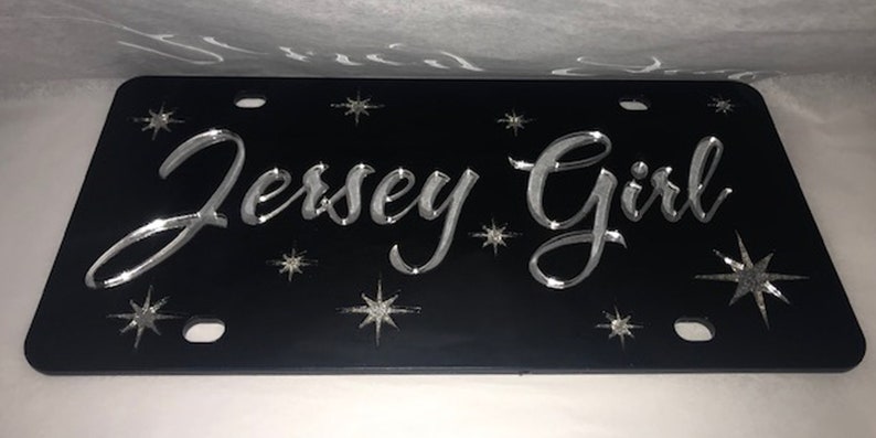 May include: Black license plate with silver lettering that reads "Jersey Girl" and silver star accents.
