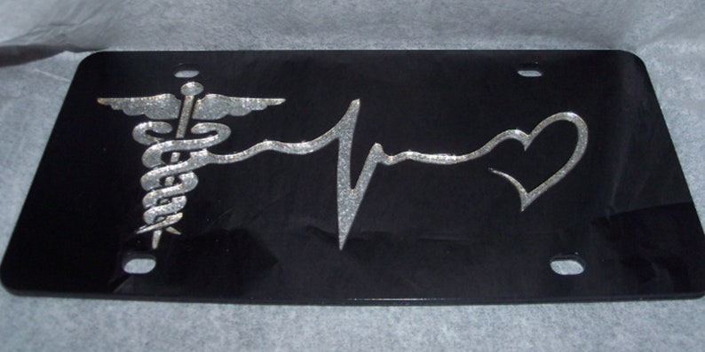 May include: Black license plate with a silver medical symbol, a silver heart, and a silver EKG line.