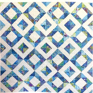 May include: A quilt featuring a repeating geometric pattern of white squares alternating with diamond-shaped blocks. The diamond blocks are composed of various blue, green, and purple patterned fabrics, creating a vibrant, multi-colored grid design.