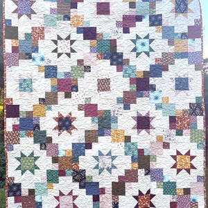 May include: A patchwork quilt featuring a repeating pattern of eight-pointed stars and small squares in various colors including maroon, mustard yellow, teal, navy, and cream. The fabric pieces are stitched together with a white background.