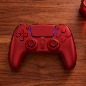 Op de afbeelding: Een metallic rode draadloze videogamecontroller met een centraal touchpad, twee analoge sticks, een richtingspad en vier actieknoppen. De controller heeft een slank, ergonomisch ontwerp met een lichtbalk geïntegreerd in het bovenste gedeelte.