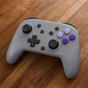 May include: A gray wireless video game controller featuring two black analog sticks, a black directional pad, and four action buttons in shades of purple and light lavender. The controller includes small black menu, home, and capture buttons.