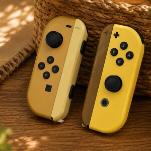 Puede incluir: Dos mandos de juego inalámbricos con un diseño bicolor. El mando izquierdo es de color amarillo mostaza y amarillo claro con un joystick y botones direccionales negros. El derecho es marrón y amarillo brillante con botones de acción negros.