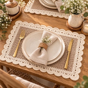 May include: A rectangular beige crochet placemat with a scalloped cream-colored border. Centered on the placemat is a round off-white plate holding a folded linen napkin secured with a woven rattan ring, flanked by a gold fork and knife.
