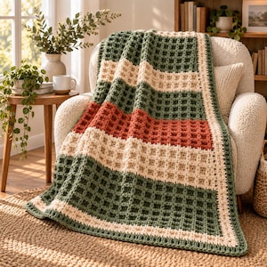 May include: A rectangular crochet blanket featuring a waffle stitch pattern with horizontal stripes in forest green, cream, and terracotta orange. The blanket is bordered by a cream-colored crochet edge that frames the entire textured design.