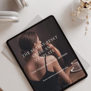 Op de afbeelding: Een digitale tablet met een voorpagina getiteld THE SUNDAY RESET GUIDE AND TEMPLATE FOR YOUNG WORKING WOMEN. Het scherm toont een persoon in een zwart topje aan een tafel met een kopje, met witte tekst over de afbeelding heen.
