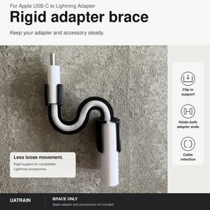 May include: A black rigid adapter brace for Apple USB-C to Lightning adapters. The device features a curved design that holds both ends of a white cable and adapter, providing clip-in support and cable retention to reduce loose movement.