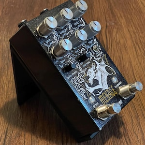 May include: A black guitar effects pedal with a glitter finish, featuring a graphic of a winged creature and the text "MENACE". It includes six silver knurled knobs, two small black knobs, a toggle switch, and two silver metal footswitches labeled "gate" and "bypass".