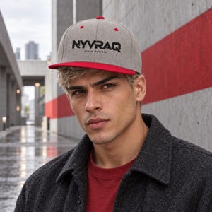 Puede incluir: Una gorra de béisbol gris jaspeado con visera plana roja y un botón superior rojo. La parte frontal de la gorra presenta el texto negro NYVRAQ con el texto negro más pequeño urban mystery impreso justo debajo en una fuente sans-serif.