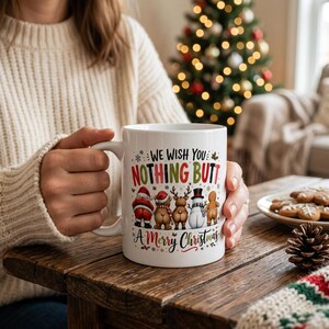 Puede incluir: Una taza de cerámica blanca con el texto WE WISH YOU NOTHING BUTT A MERRY CHRISTMAS en rojo, verde y negro. El diseño incluye ilustraciones de Santa, un oso, un reno, un muñeco de nieve y un hombre de jengibre vistos de espaldas.