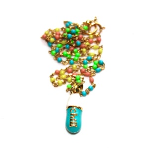 May include: A gold chain necklace with a blue and white pill charm that says "Chill". The chain is made of small, colorful beads in shades of pink, yellow, green, and blue.