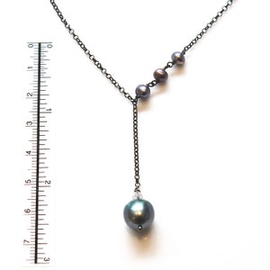 May include: A black chain necklace with a single large dark gray pearl pendant and three smaller dark gray pearls on the chain.