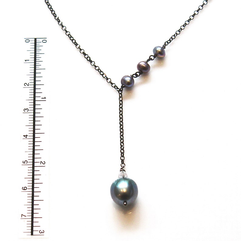 May include: A black chain necklace with a single large dark gray pearl pendant and three smaller dark gray pearls on the chain.