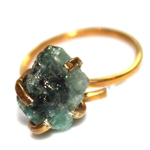 Pu&ograve; includere: Un anello d'oro con una pietra preziosa di smeraldo grezzo. Lo smeraldo &egrave; di colore verde scuro e ha una texture ruvida e naturale. L'anello &egrave; semplice ed elegante.