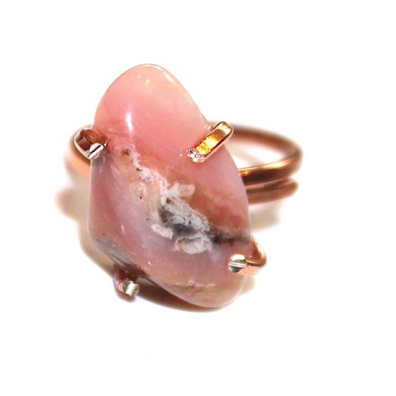 May include: A pink opal ring with a rose gold band. The opal is a natural stone with a unique pattern and colour.