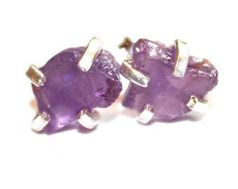 May include: A pair of amethyst earrings with silver settings. The amethyst stones are raw and have a purple hue.