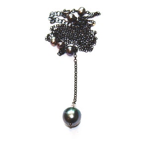 May include: A black chain necklace with a single large black pearl pendant and smaller black pearls along the chain.