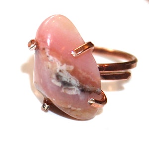 May include: A pink opal ring with a copper band. The opal is a freeform shape with a natural, organic look. The copper band is simple and elegant.