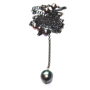 May include: A black chain necklace with a long drop featuring a large, dark green pearl. The necklace is adorned with several smaller pearls.