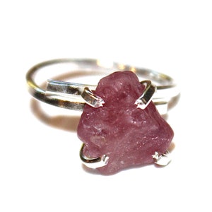 May include: A silver ring with a pink gemstone set in the center. The gemstone is a rough, natural shape and is held in place by silver prongs.