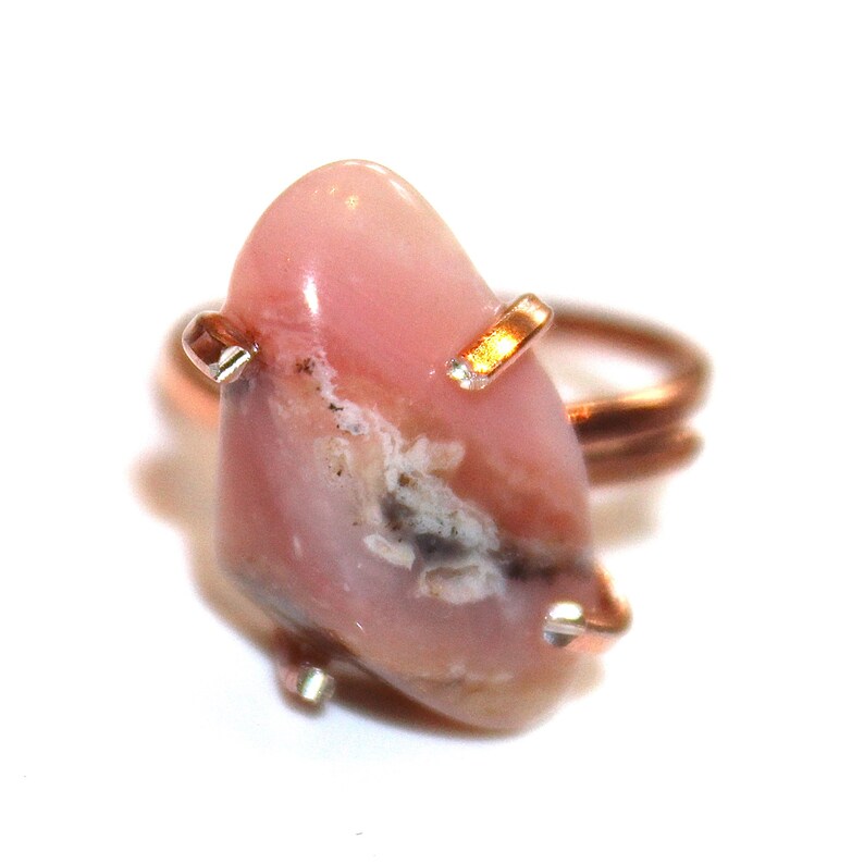May include: A pink opal ring with a copper band and gold accents. The opal is a natural stone with a unique pattern and colour.