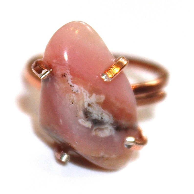 May include: A pink and white opal ring set in copper wire. The ring is handmade and features a unique, natural stone.
