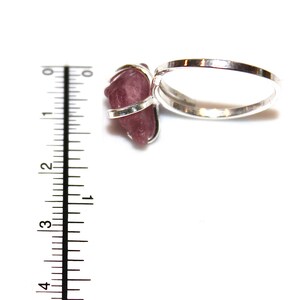 May include: A silver ring with a pink crystal stone set in a wire wrap. The ring is shown next to a ruler, with the stone measuring approximately 2.5 cm in length.