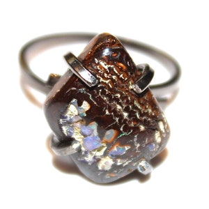 May include: A silver ring with a brown and iridescent opal gemstone set in a bezel setting. The opal has a unique pattern of white, blue, and green.