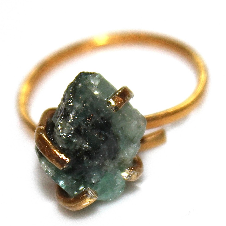 Pu&ograve; includere: Un anello d'oro con un grande smeraldo verde grezzo incastonato al centro. Lo smeraldo &egrave; tenuto in posizione da un filo d'oro.
