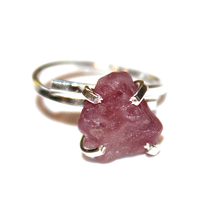 May include: A silver ring with a pink, rough-cut gemstone set in the centre.