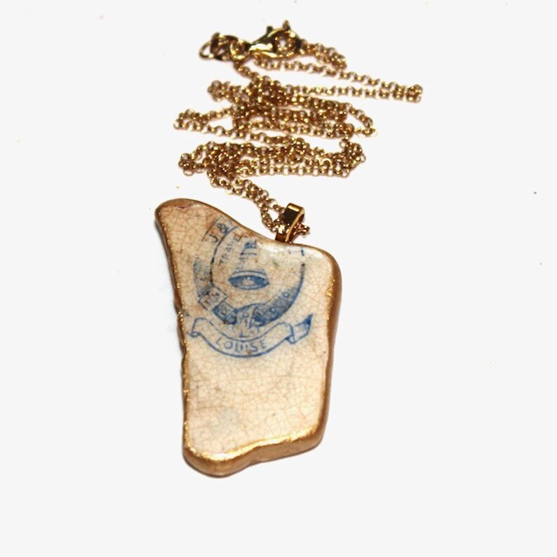 May include: A gold chain necklace with a white ceramic pendant featuring a blue and white design with the text "The Franklin Fire Co. No. 1 Louise".
