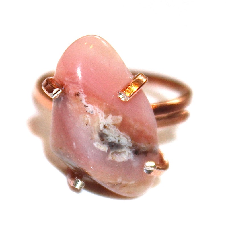 May include: A pink opal ring set in copper wire with gold accents. The opal has a unique pattern of white and grey inclusions.