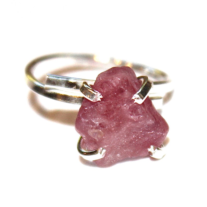 May include: A silver ring featuring a pink gemstone set in a simple, modern design.