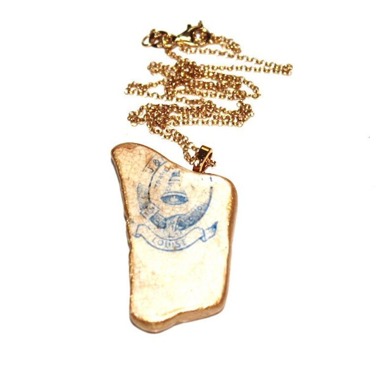 May include: A gold chain necklace with a pendant featuring a vintage-style stamp with blue ink. The stamp reads "TRADE MARK" and "LOUISE".