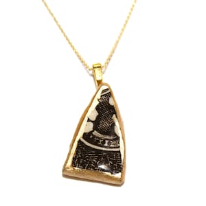 May include: A gold chain necklace with a triangular pendant. The pendant is made of ceramic and has a black and white design with gold accents.