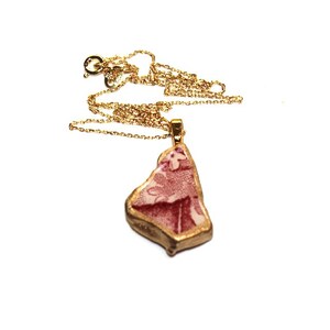 May include: A gold chain necklace with a pendant made from a piece of broken china with a pink and white floral pattern. The china is framed with gold paint.
