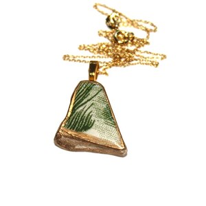 May include: A gold chain necklace with a pendant made from a piece of broken pottery with a green and white design.