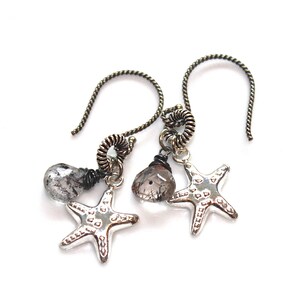 May include: Silver earrings with a dangling clear quartz stone and a silver starfish charm. The earrings are made with a twisted wire design.