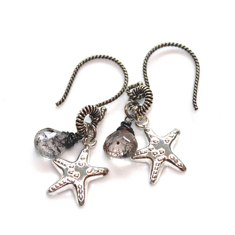 May include: Silver earrings with a dangling clear quartz stone and a silver starfish charm. The earrings are made with a twisted wire design.