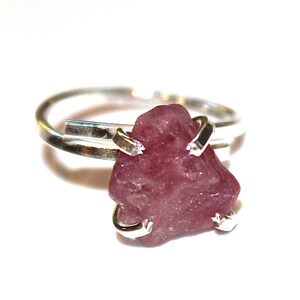 May include: A silver ring featuring a pink gemstone set in a simple, modern design. The gemstone is a rough, natural shape and is held in place by silver prongs.