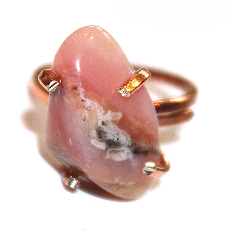 May include: A pink opal ring with copper wire wrapping. The opal has a unique pattern of white and grey inclusions.