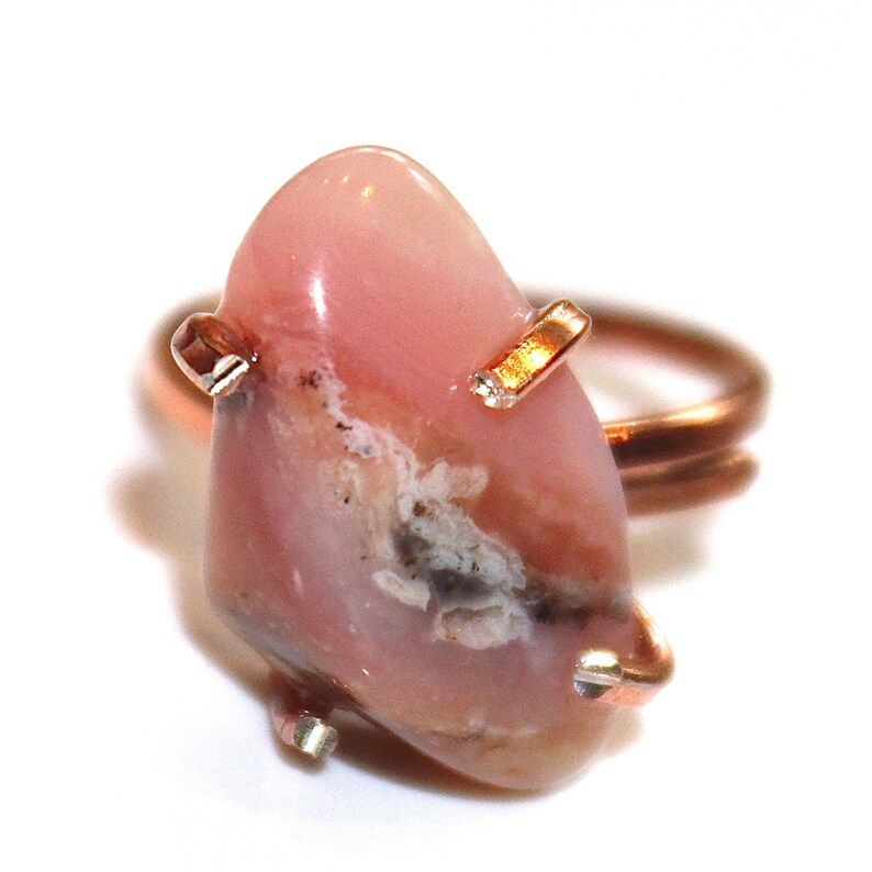 May include: A pink opal ring with copper wire wrapping. The opal has a unique pattern of white and grey inclusions.