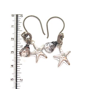 May include: Silver dangle earrings with a silver starfish charm, a clear quartz stone, and a silver wire wrapped loop. The earrings are hanging from a silver wire.