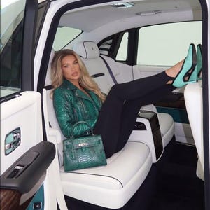 May include: A green snakeskin-textured leather jacket, a matching green snakeskin-textured handbag with a silver-tone clasp, black leggings, and light green pointed-toe heels with black trim, all worn inside a vehicle with white leather seats.