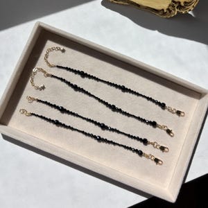 May include: Four delicate bracelets featuring small, faceted black beads strung on gold-toned chains. Each bracelet includes a gold-toned lobster clasp and an adjustable extension chain finished with a tiny star-shaped charm at the end of the chain.