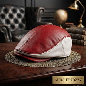 Puede incluir: Una gorra plana de dos tonos confeccionada en cuero, con un panel superior de color rojo intenso y una sección inferior blanca en contraste. La gorra presenta una corona redondeada estructurada y una visera corta y rígida con costuras visibles.