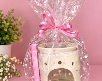 May include: A ceramic wax warmer with a speckled cream finish and a large arched opening, packaged in clear cellophane wrap with pink polka dots and tied at the top with a pink ribbon, accompanied by a long, thin pink wax melt bar.